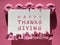 Text Happy Thanksgiving in frame. Pink fuchsia paper background with Autumn decor.