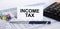 Text Income Tax on white card with blue metal pen, calculator and paper clips on financial table