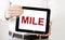 Text MILE on tablet display in businessman hands on the white bakcground. Business concept
