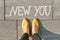 Text new you written on gray sidewalk with women legs, top view