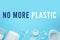 Text NO MORE PLASTIC and different disposable dishware on light blue background, flat lay