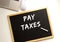 Text PAY TAXES written in chalk on a slate board. Office desk