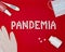 Text phrase Pandemia on a red background with medicines, hand antiseptic, thermometer and protective mask