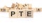text PTE - Pearson Tests of English - is written on three wooden cubes standing on a white table. in the background - a