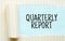 The text QUARTERLY REPORT appearing behind torn white paper