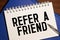 Text Refer a friend written on the white paper with pen and a cup of coffee aside