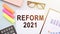The text Reform 2021 on office desk with calculator, markers, glasses and financial charts
