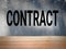 Text says Contract on cement wall background.  CONTRACT, text on concrete wall background with wood plank as a frame.