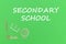 Text secondary school, school supplies wooden miniatures on green background
