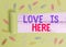 Text sign showing Love Is Here. Conceptual photo Roanalysistic feeling Lovely emotion Positive Expression Care Joy Paper