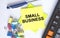 Text Small Business on yellow stickers with calculator, blue pen and paper clips