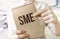 Text SME SMALL MEDIUM ENTERPRISES on brown paper notepad in businessman hands in office. Business concept