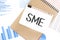 Text SME SMALL MEDIUM ENTERPRISES on white paper sheet and brown paper notepad on the table with diagram. Business concept