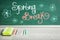 Text Spring Break and flower drawings on green chalkboard near wooden table. School holiday