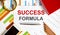 Text SUCCESS FORMULA on the notepad with office tools, pen on financial report