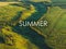 Text SUMMER above aerial view photo of green hills, fields and meadows with forest in sunset light, summertime concept