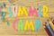 Text SUMMER CAMP of multicolored paper letters and color pencils on a natural wooden background. top view. flat lay