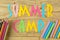 Text SUMMER CAMP of multicolored paper letters and color pencils on a natural wooden background. top view. flat lay