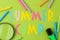 Text SUMMER CAMP of multicolored paper letters and colored crayons on a bright green background. top view. flat lay