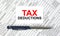 Text Tax Deductions written on a business card lying on financial tables with a blue metal pen