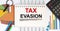 Text Tax Evasion on notepad with office tools, pen on financial report