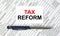 Text Tax Reform written on a business card lying on financial tables with a blue metal pen