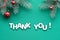 Text Thank you on turquoise Christmas textile background. Top view on fir twigs decorated with red glass baubles