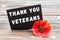 The text thank you veterans written in a chalkboard and red poppy on a rustic wooden background.