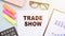 The text - TRADE SHOW on office desk with calculator, markers, glasses and financial charts