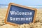 Text welcome summer in a chalkboard, on the sand of a beach