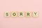 Text wooden blocks spelling the word sorry on pink background