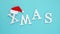 Text Xmas from volume white letters in red Santa hat and falling snow on blue background. Concept Merry christmas. Top