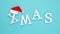 Text Xmas from volume white letters in red Santa hat and falling snow on blue background. Concept Merry christmas. Top view Flat l