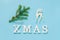 Text Xmas from white letters, green fir branch and christmas decoration deer toy on blue background. Concept Merry christmas.