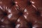 The texture of the background is a close-up of brown genuine leather, upholstered furniture in retro Chesterfield style