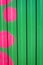 The texture of a bright colored wall, a green embossed fence with bright pink circles painted on it, vertical format