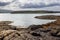 Textured rocks and rich marine flora frame the peaceful expanse of sea leading to rolling hills under a soft sky near Skye