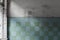 Textured wall of an abandoned building, lined with glossy square ceramic turquoise tiles with the sun\\\'s rays on the wall