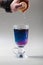 Thai blue butterfly pea tea in an Irish glass. Gray background. Hand is squeezing lemon slice. Blue tea Anchan, Clitoria