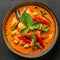 Thai cuisine. Bowl of tasty red curry on dark table. Vegetables, spices, rice, tofu.