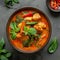 Thai cuisine. Bowl of tasty red curry on dark table. Vegetables, spices, rice, tofu.