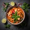 Thai cuisine. Bowl of tasty red curry on dark table. Vegetables, spices, rice, tofu.