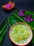 Thai dessert in a bowl with coconut pandan leaves as a black background element.