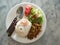 Thai food - spicy stirred fried pork chop served with rice, fried egg, and vegetables on a white dish on a white marble table