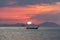 Thai longtail boat in the sea at sunset with big red sun and mountains silhouettes and clouds