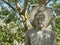 Thai sitting Buddha sculpture statue  surrounded by natural green trees forest background on sunny day.