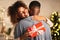 Thankful afro woman with christmas gift hugging husband at home