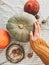 Thanksgiving concept. Hand in yellow sweater holding pumpkin and nuts,  flowers, fall leaves on rustic table, flat lay. Fall decor