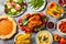 Thanksgiving dinner table with roasted whole chicken or turkey, green beans, mashed potatoes, cranberry sauce, grilled vegetables