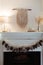 Thanksgiving home  decor - white wooden fireplace with wall macrame, cream and beige pumpkins, pine cones garland and rustic dry